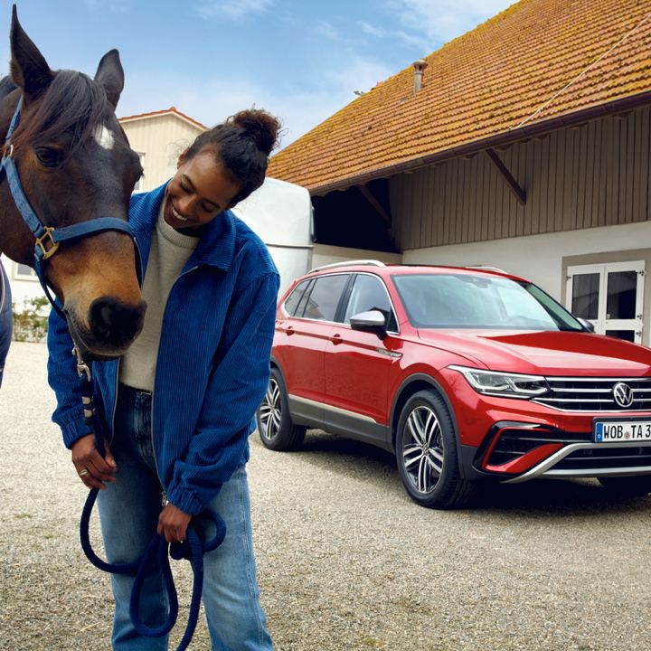 Un chico con un caballo y un Volkswagen SUV rojo al fondo