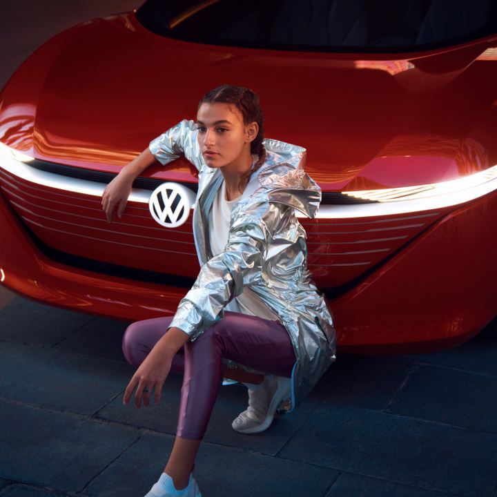 Chica de rodillas delante del frontal de un Volkswagen.