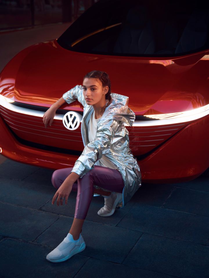 Chica de rodillas delante del frontal de un Volkswagen.
