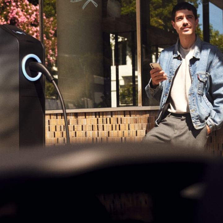 Un chico visto desde el interior de un Volkswagen con un teléfono móvil junto a una estación de carga