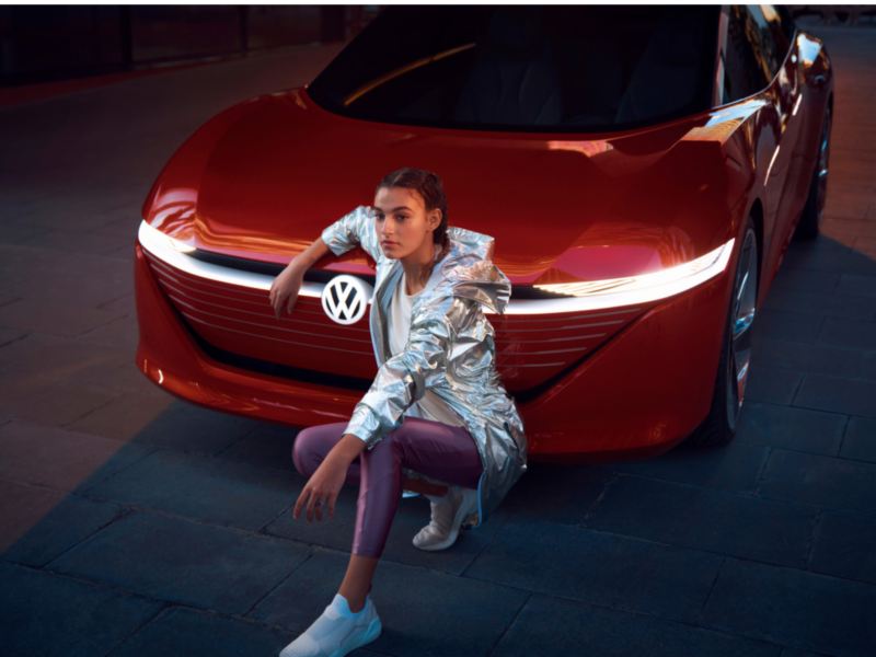 Una chica agachada y apoyada en al capó de un Volkswagen ID. Vizzion