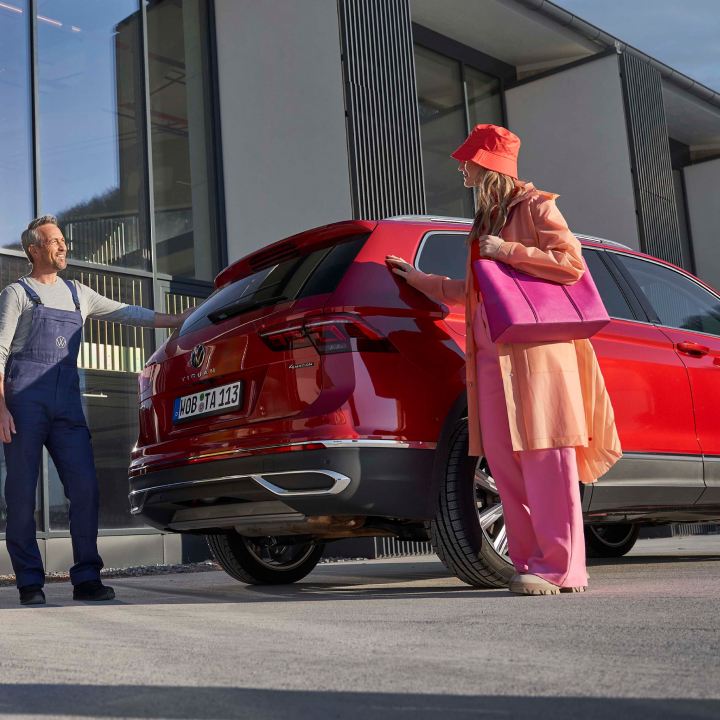 Agente de servicio de Volkswagen con una chica de pie detrás de un Volkswagen Tiguan rojo