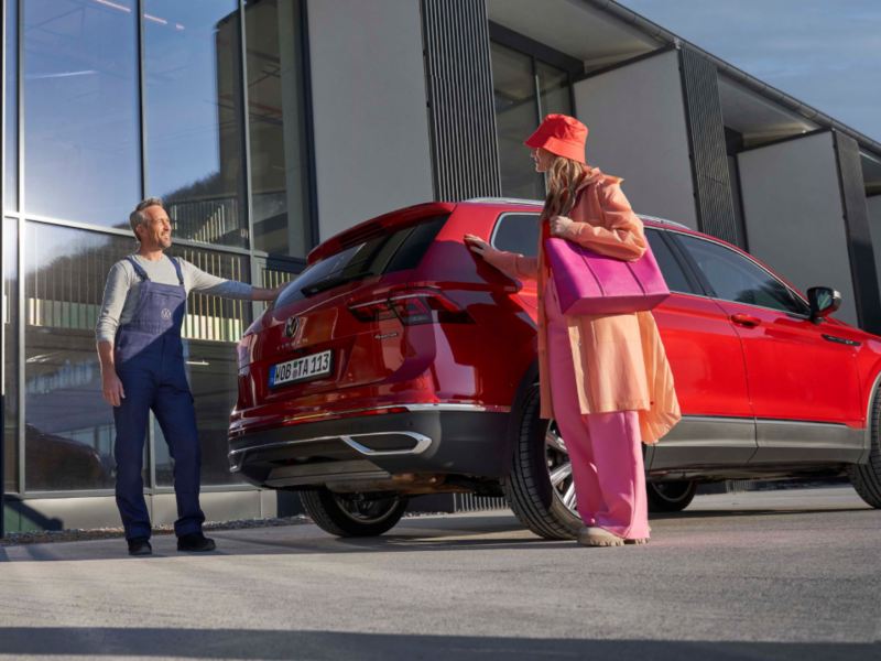 Agente de servicio de Volkswagen con una chica de pie detrás de un Volkswagen Tiguan rojo