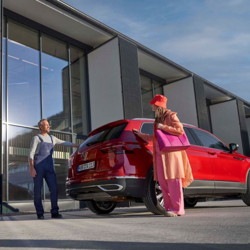 Una mujer y un agente de servicio Volkswagen junto a un Tiguan rojo frente a una instalación
