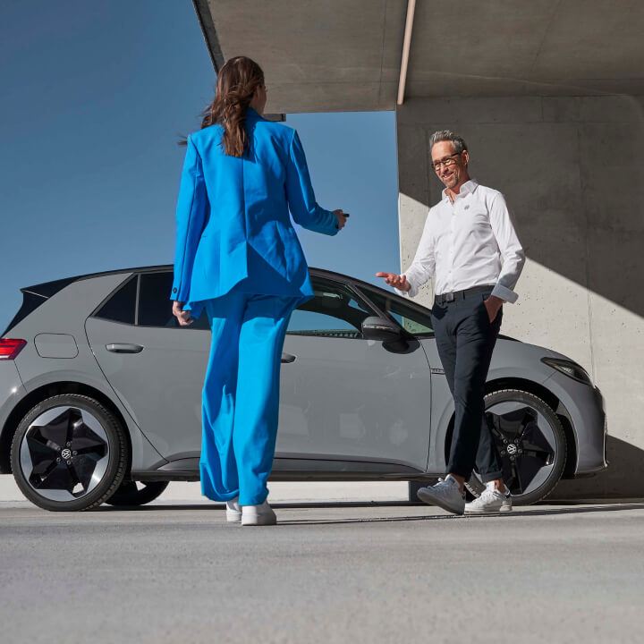 Una pareja al lado de un Volkswagen de color gris estacionado