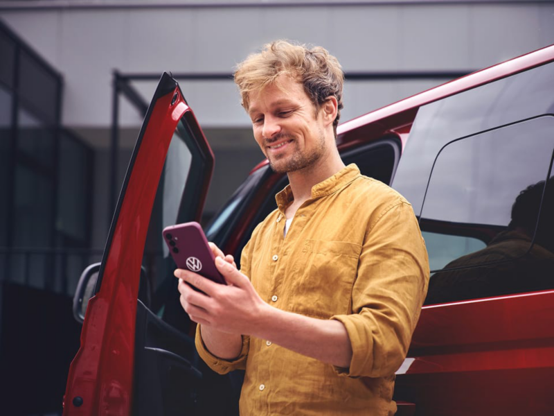 Una persona mirando el móvil junto a una furgo de VW roja.
