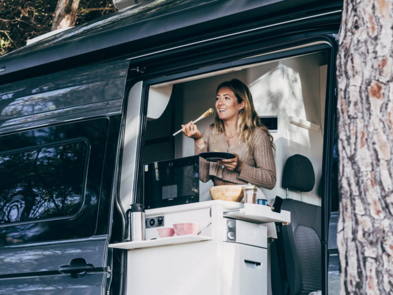 Una persona cocinando en su furgo Volkswagen aparcada en un espacio natural