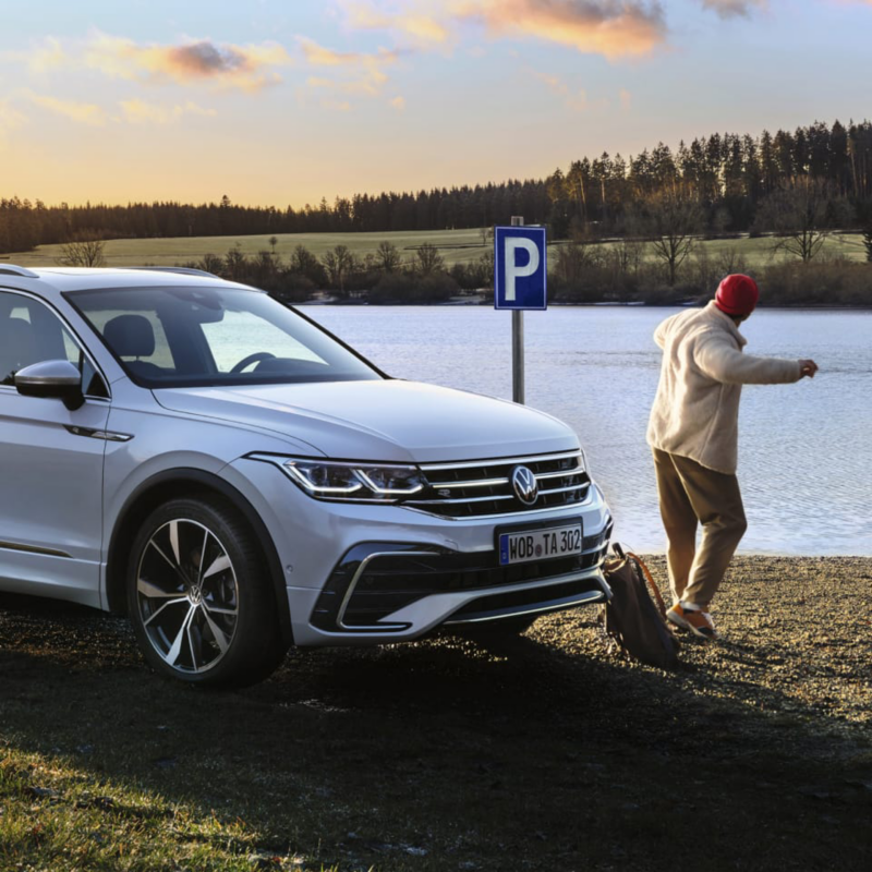 Un chico delante de un Volkswagen Tiguan Allspace de color blanco junto a un lago