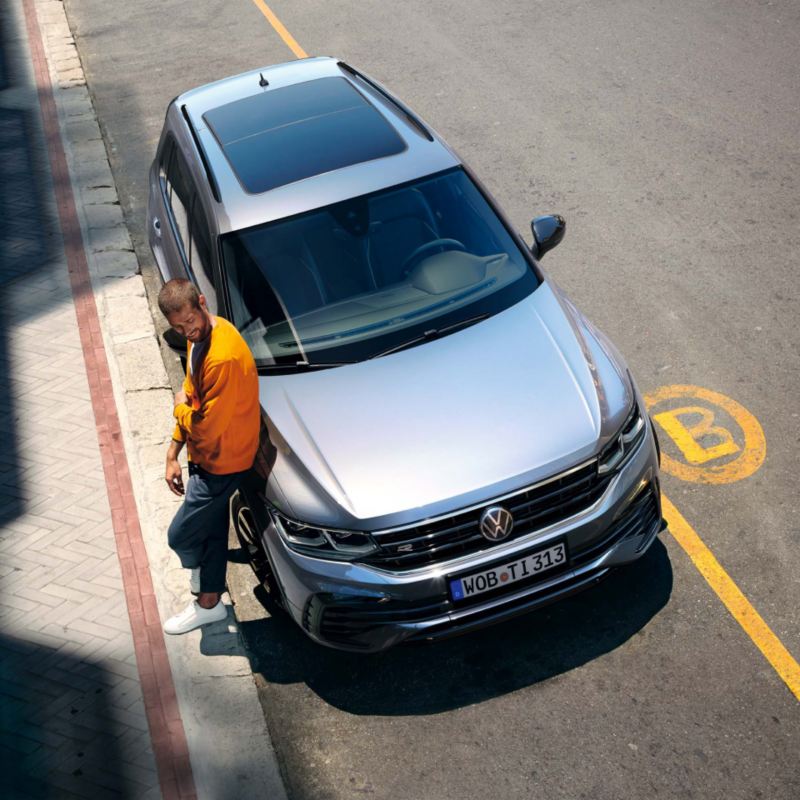 Chico de pie apoyado a un Nuevo Volkswagen Tiguan aparcado en la calle