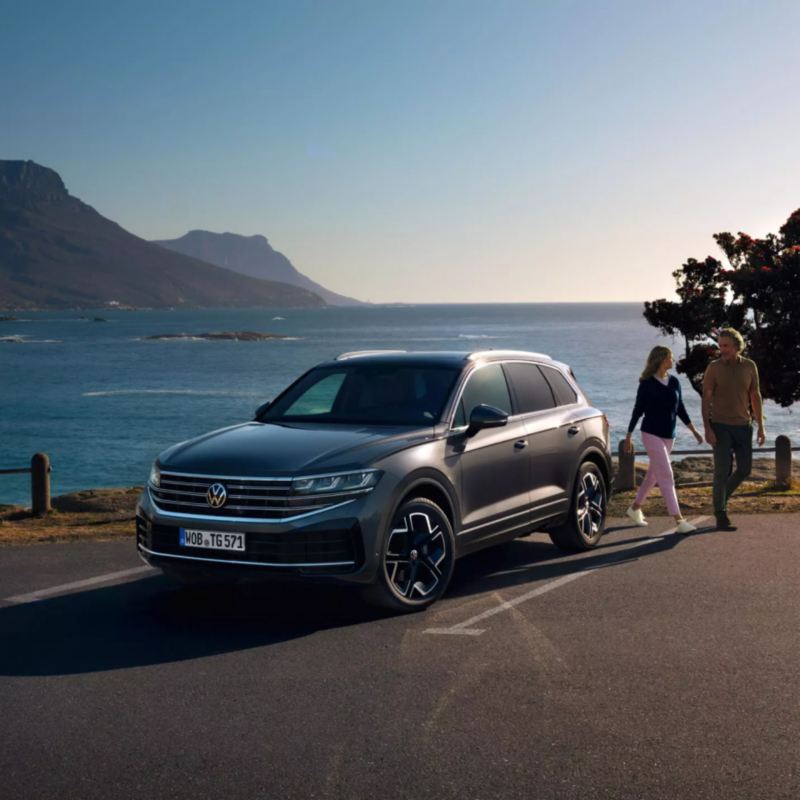 Una pareja junto a un Volkswagen Touareg estacionado frente al mar