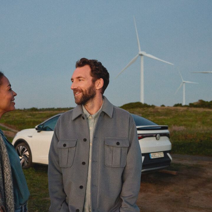 pareja junto a un Volkswagen estacionado en un campo con molinos de viento