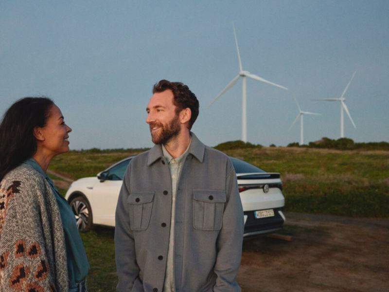 pareja junto a un Volkswagen estacionado en un campo con molinos de viento