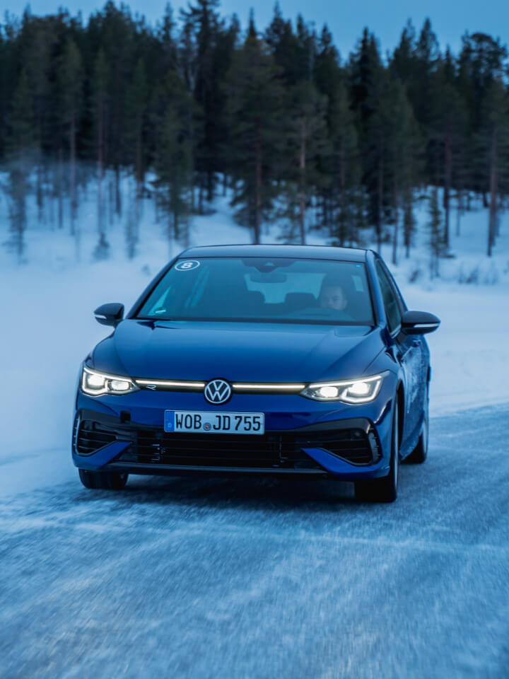 Vista frontal de un Golf R azul circulando en una carretera con nieve