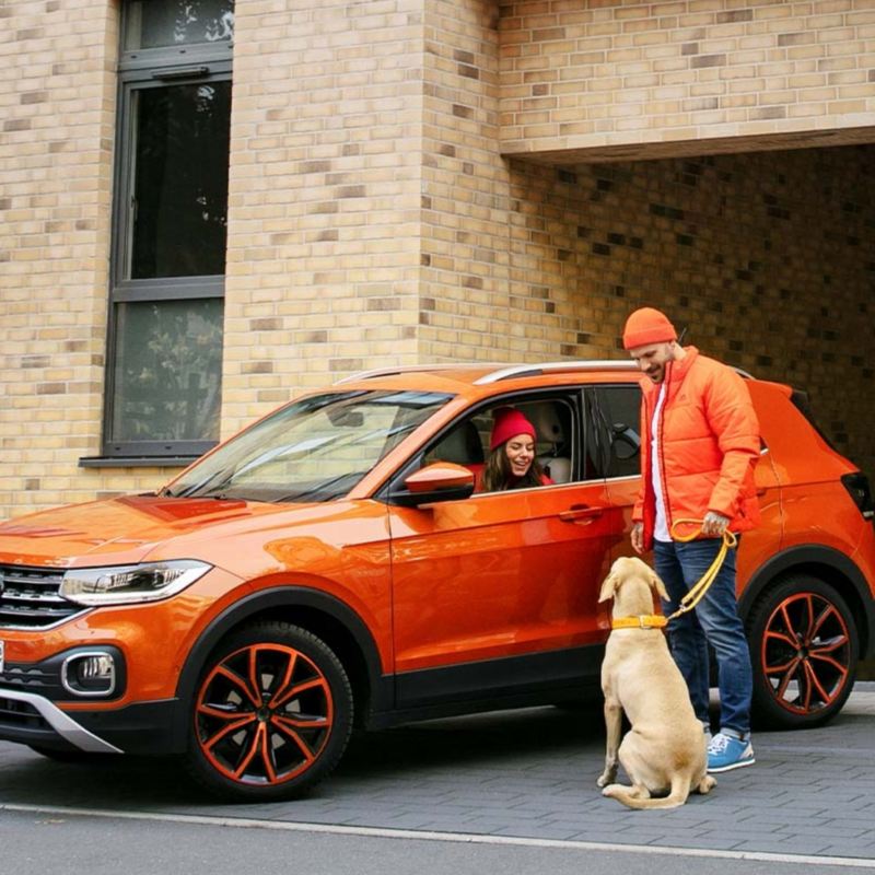 Chica de un Volkswagen T-Cross naranja sonriendo a un perro acompañado de un hombre