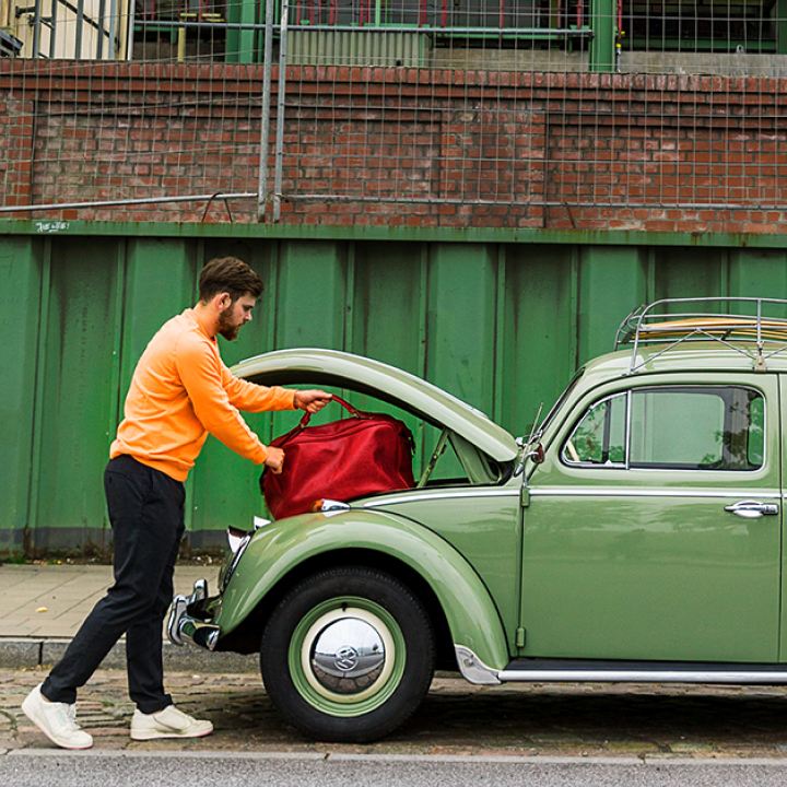 Hombre cargando una maleta en su Volkswagen Bettle verde en la ciudad