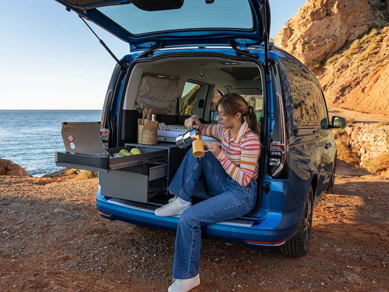 Una persona tomando café en la puerta trasera de su furgo Volkswagen