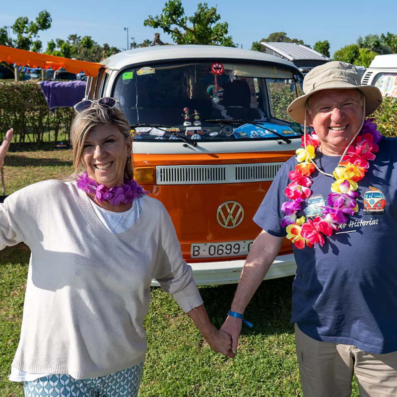 Dos personas con aires festivos delante de su furgo Volkswagen clásica