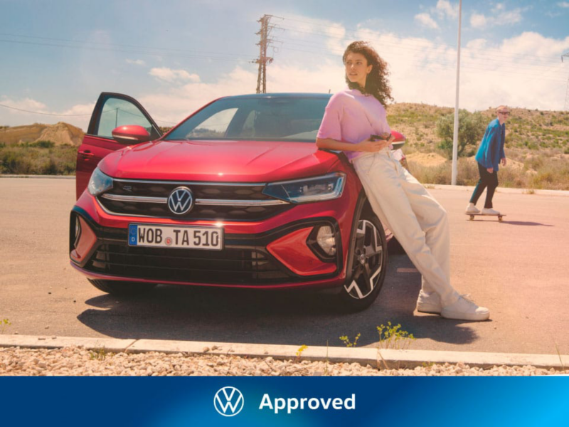 Una chica apoyada en un Volkswagen Taigo de color rojo con el logo de Approved
