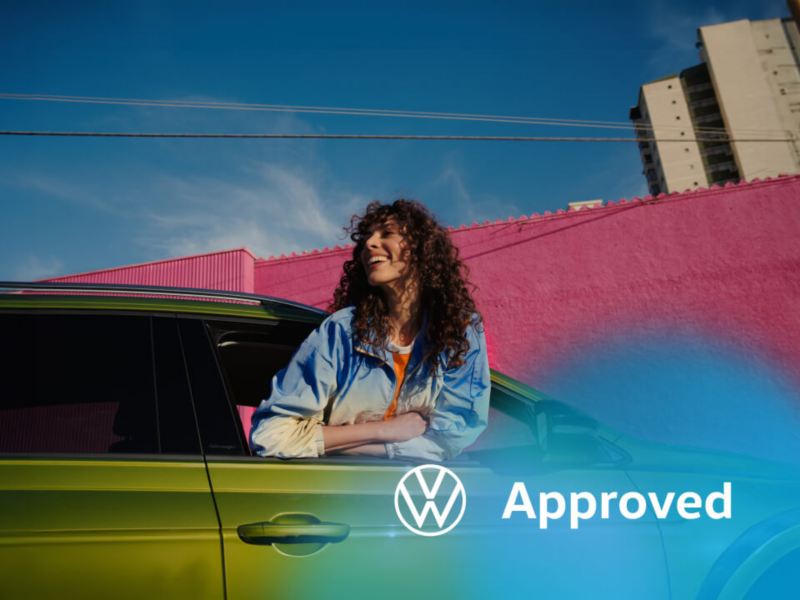 Una chica en la ventana de un Volkswagen de color verde con el logo de Approved