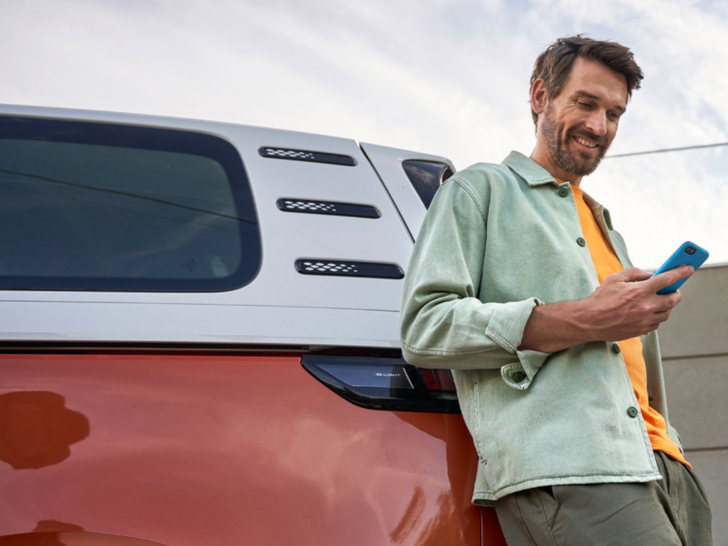 Un hombre con un smartphone apoyado sobre un Volkswagen ID. Buzz