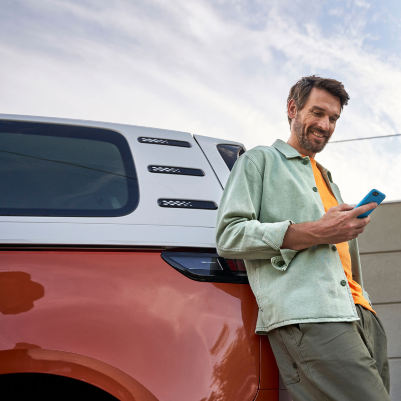 Un hombre de pie con su móvil en la mano apoyado en una ID.Buzz aparcada en la calle