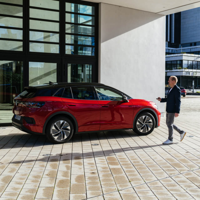 Un hombre junto a un Volkswagen de color rojo estacionado fuera de un edificio