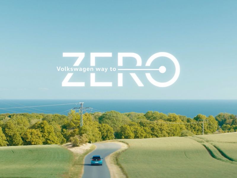 Volkswagen circulando por una carretera rodeada de campos con el logo sobreimpreso Way to zero de Volkswagen