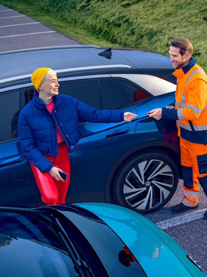 Una chica apoyada en un Volkswagen ID.4 azul recibiendo las llaves de un agente de servicio