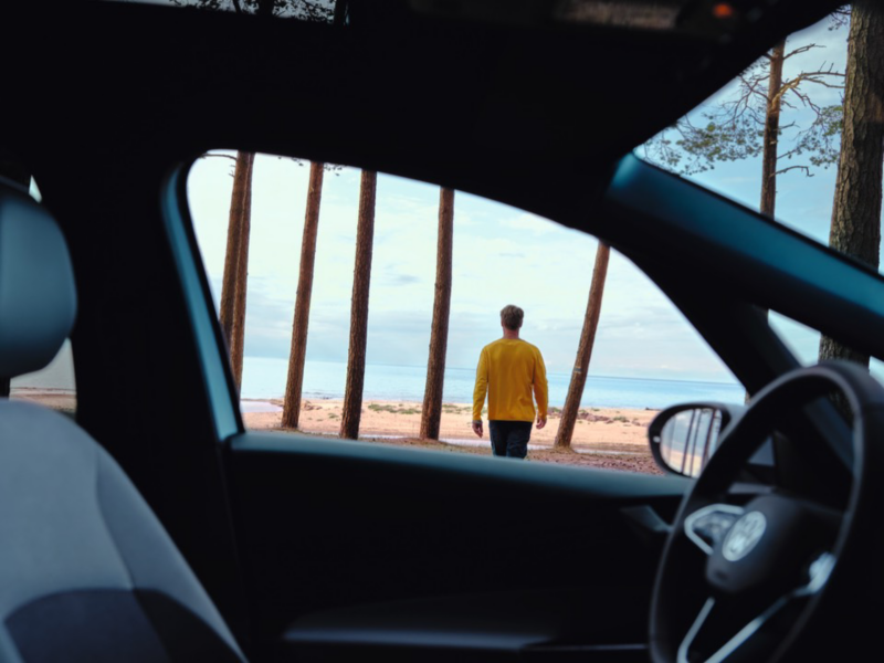 Hombre de espaldas caminado hacia el mar visto desde el interior de un Volkswagen