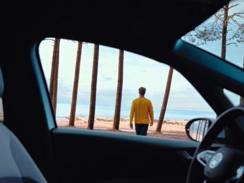 Hombre de espaldas caminado hacia el mar visto desde el interior de un Volkswagen