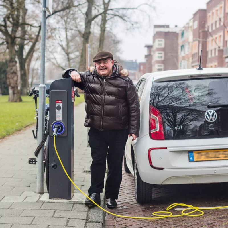 Hombre mirando la cámara cargando un e-Up! de Volkswagen en la calle