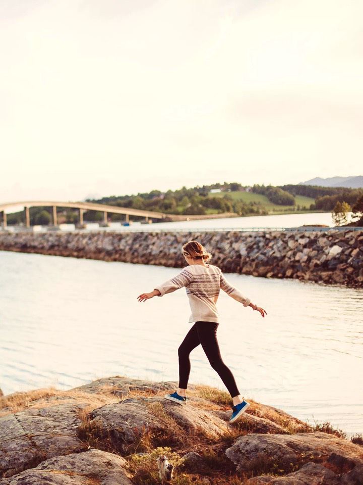 Chica andando con los brazos en alto por las rocas en la orilla del mar al atardecer