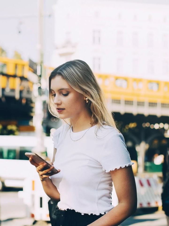 Chica vestida de blanco mirando el móvil en la ciudad