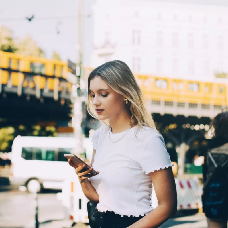 Chica vestida de blanco mirando el móvil en la ciudad