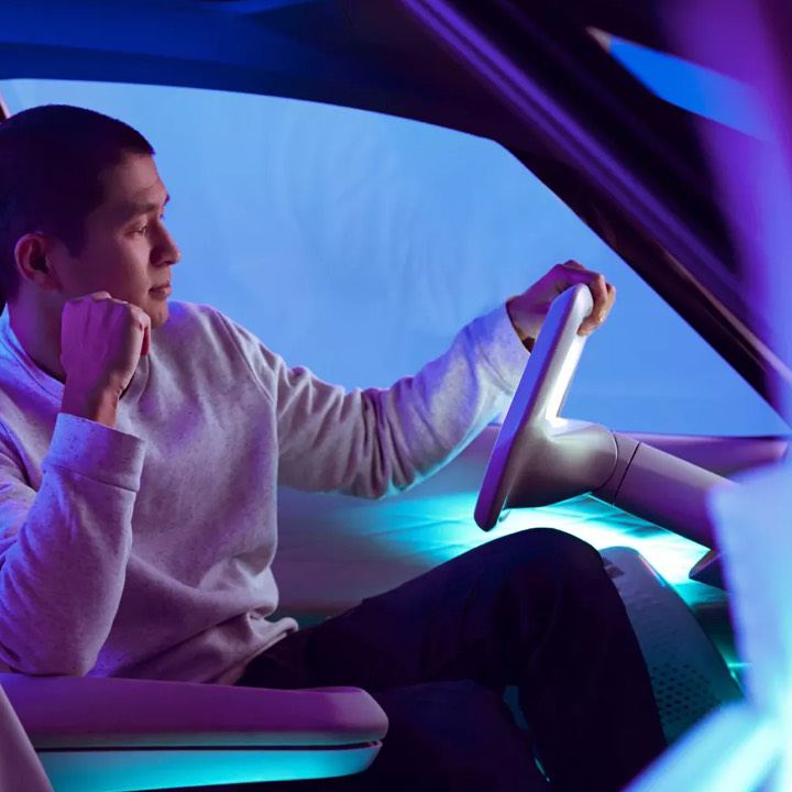 Hombre al volante de un Volkswagen eléctrico visto de lado e iluminado por luces azules