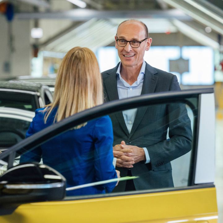 Un hombre y una mujer hablando junto a un Volkswagen ID.4 amarillo con la puerta abierta