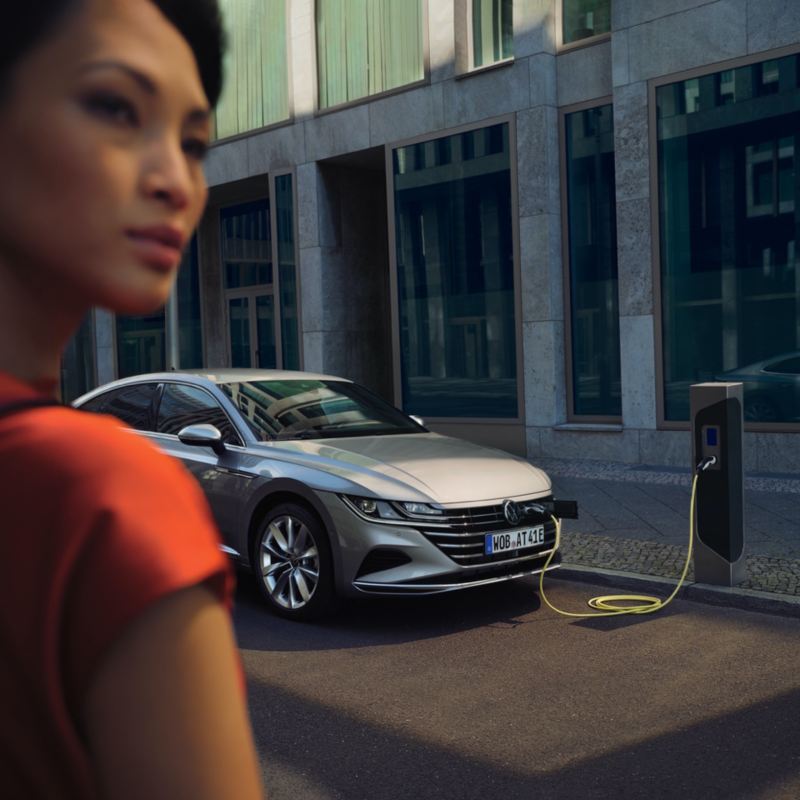 Chica en primer plano delante de un Volkswagen conectado a un cargador eléctrico