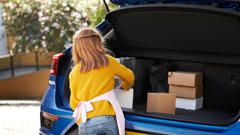 A young girl loading cardboard boxes into the boot of a blue Volkswagen