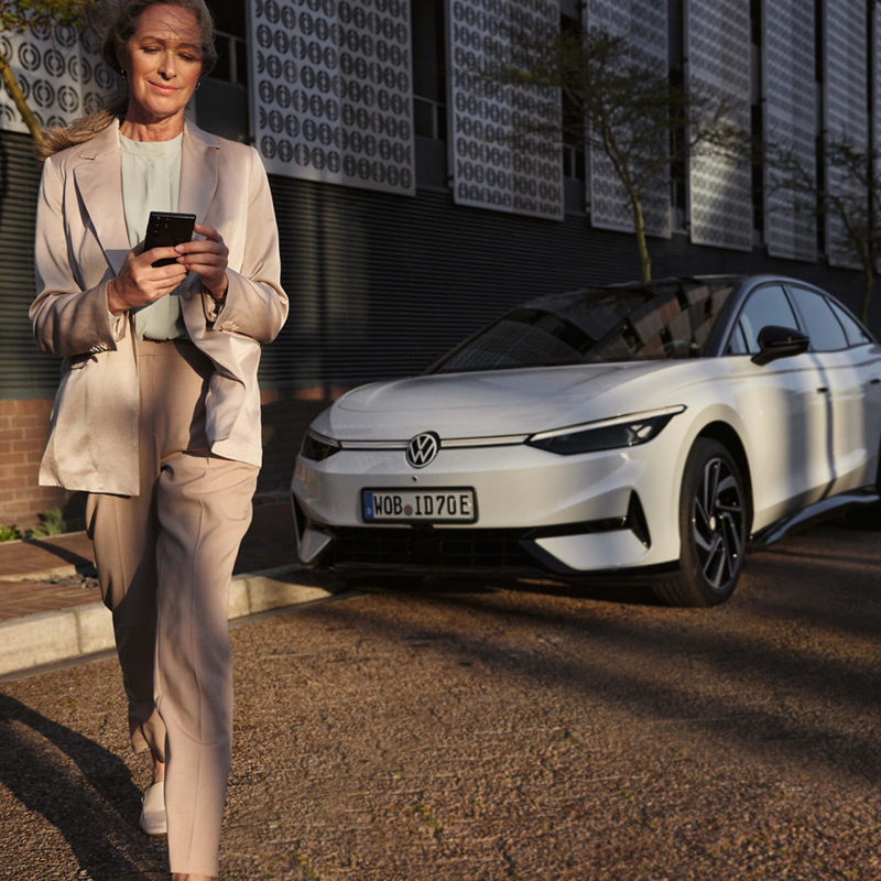 A woman walking away from a white VW while looking at a smartphone