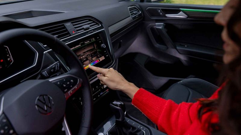 Mujer que conduce un Volkswagen toca con un dedo la pantalla táctil de su auto. 
