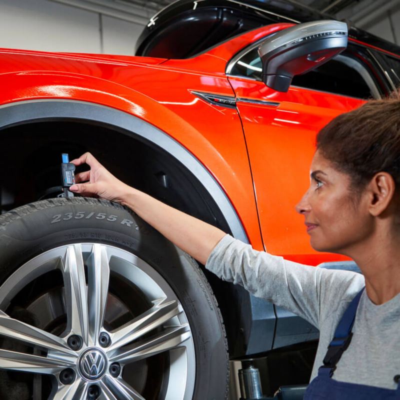 Une technicienne Volkswagen contrôle l'usure des pneumatiques avant d'un Tiguan.