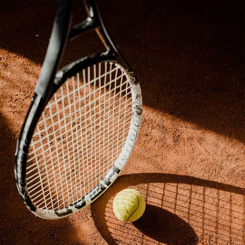 Raqueta de tenis con pelota en el suelo. Elementos del Campeonato Nacional Juvenil de Tenis.