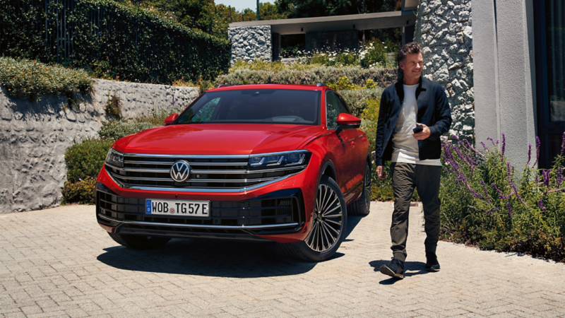 Ein Mann läuft an einem roten VW Touareg R eHybrid vorbei.