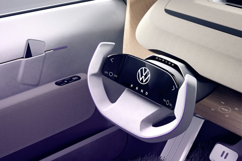 Vista parziale della postazione di guida di Volkswagen ID. LIFE, con volante sensibile al tocco, comandi automatici per il finestrino, porta cellulare e pedali.