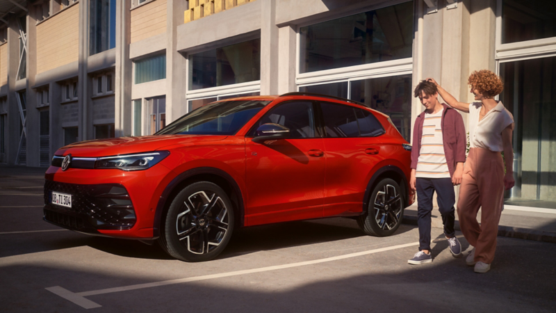 A side shot of a red Tiguan parked outside an office and 2 people standing close to the car