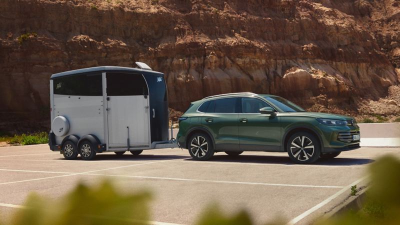 Dark green VW Tiguan with horse trailer parked in front of a rocky landscape.