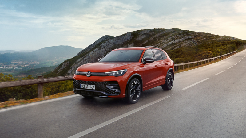 a red New Tiguan driving along a mountain lined road