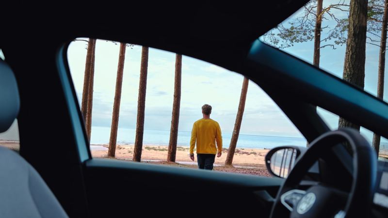 The view from a car of a man walking towards a sea.
