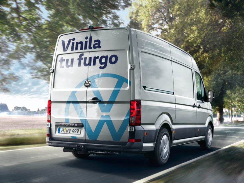 Plano trasero de una furgo Volkswagen en carretera con un vinilo que dice Vinila tu furgo