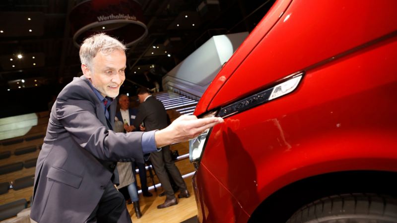 Thomas Sedran pekar på framlampan på en röd VW Multivan T6.1